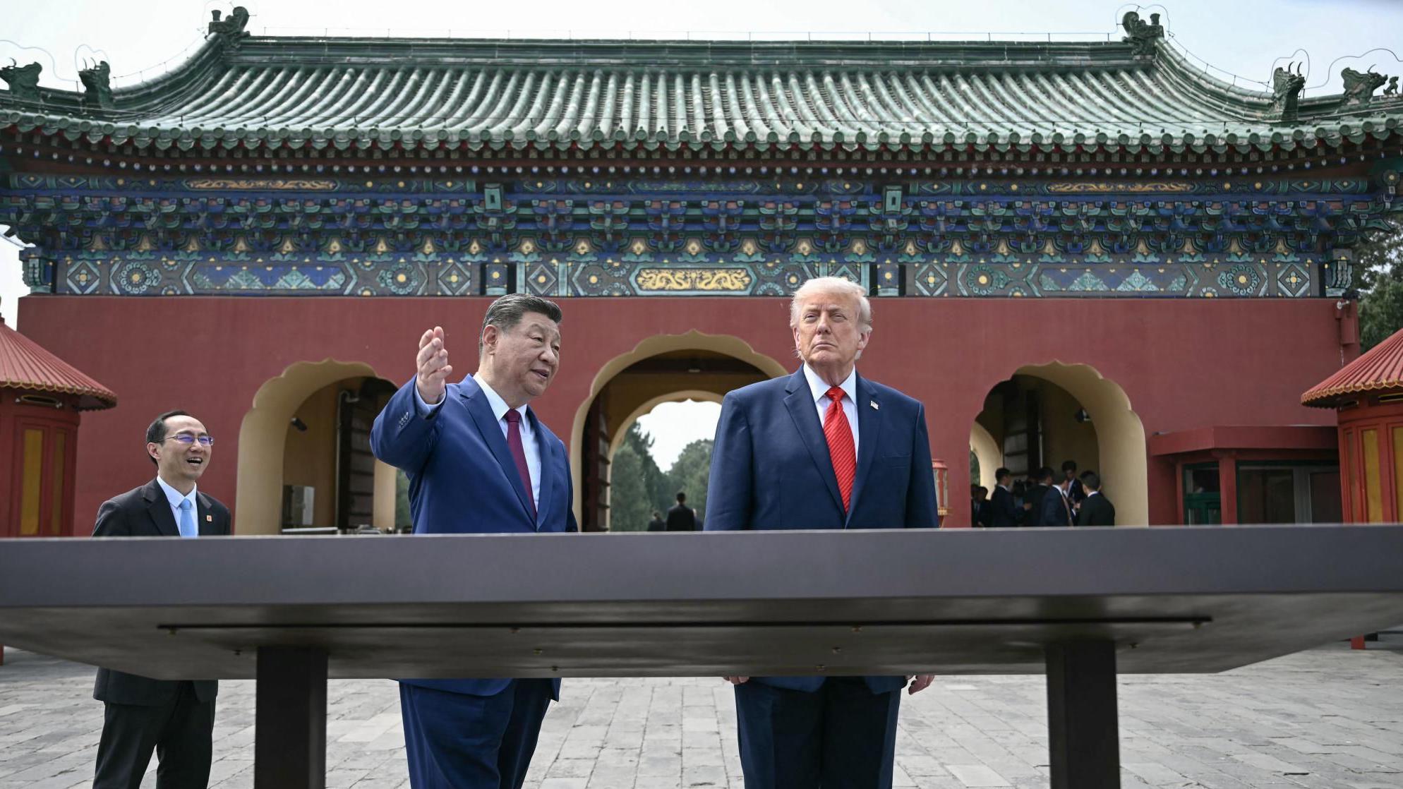 Los presidentes Xi y Trump se encuentran en el patio de un complejo templario, detrás de una gran exhibición, con Xi levantando la mano para mostrarle algo a Trump.