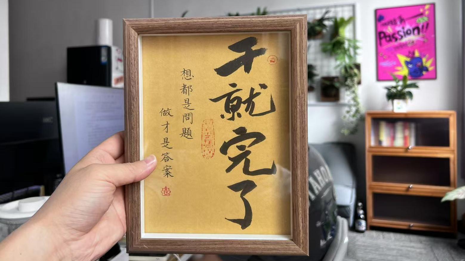 桌上一處相框裡印著：「乾就完了」幾個大字，旁邊小字寫著「想都是問題，做才是答案」。