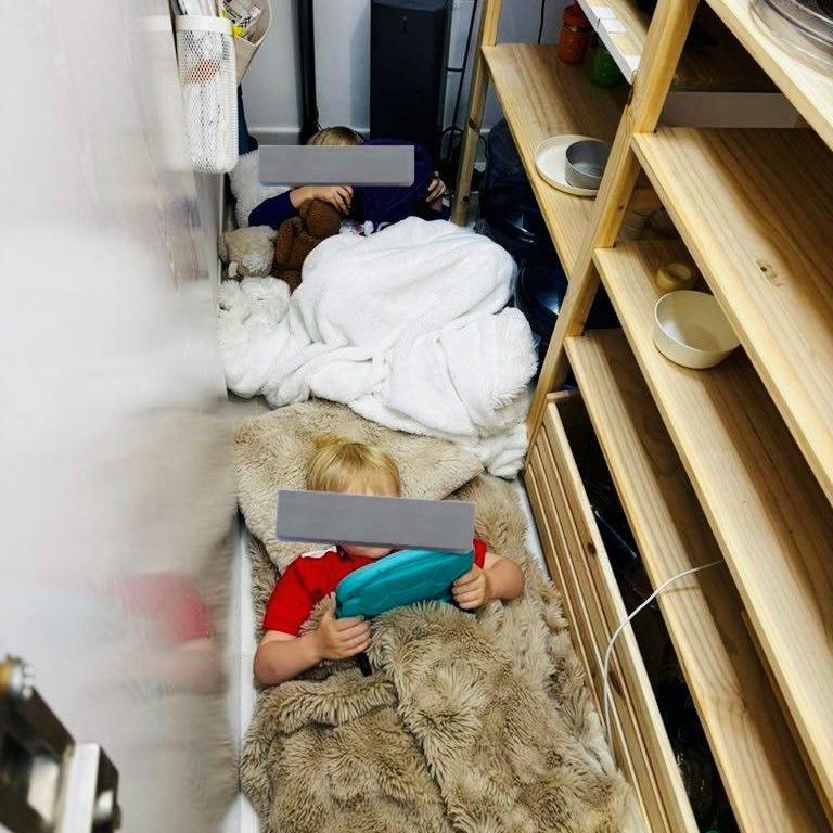Dos niños pequeños con el rostro oculto (por unas barras grises) bajo unas mantas dentro de un armario.