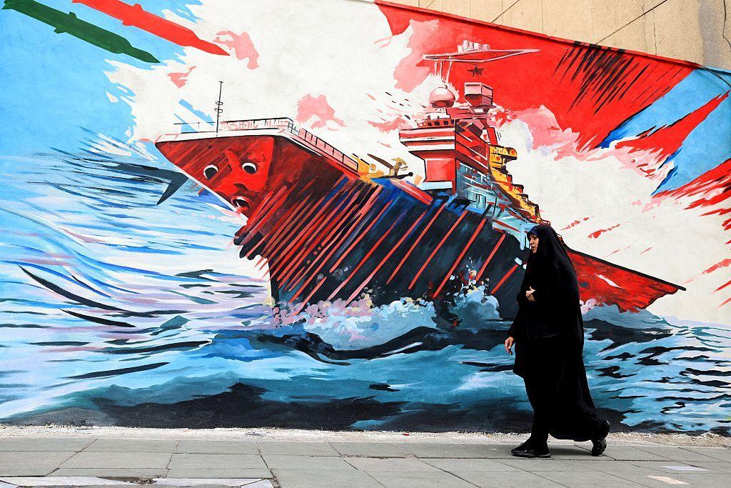 Una mujer pasa junto a un mural de propaganda iraní en Teherán. El mural muestra misiles con los colores de la bandera de Irán dirigiéndose contra un barco de guerra. 