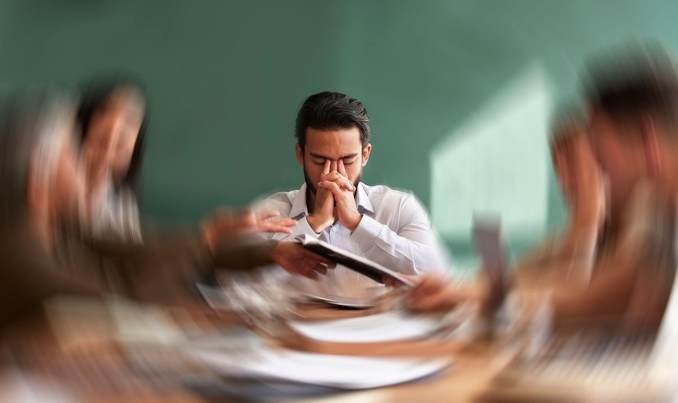 Homem com semblante tenso em reunião de trabalho com a demais pessoas desfocadas à sua volta