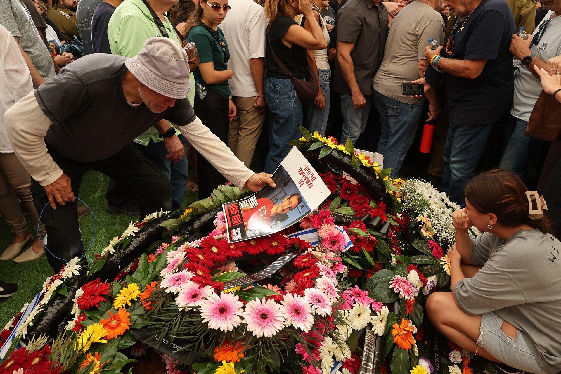 Una persona sostiene la foto de Tamir Nimrodi, un soldado israelí que murió en cautiverio en Gaza tras ser capturado en octubre de 2023, que yace sobre un montón de flores rodeado de dolientes en la ciudad central israelí de Kfar Saba.16 de octubre de 2025.