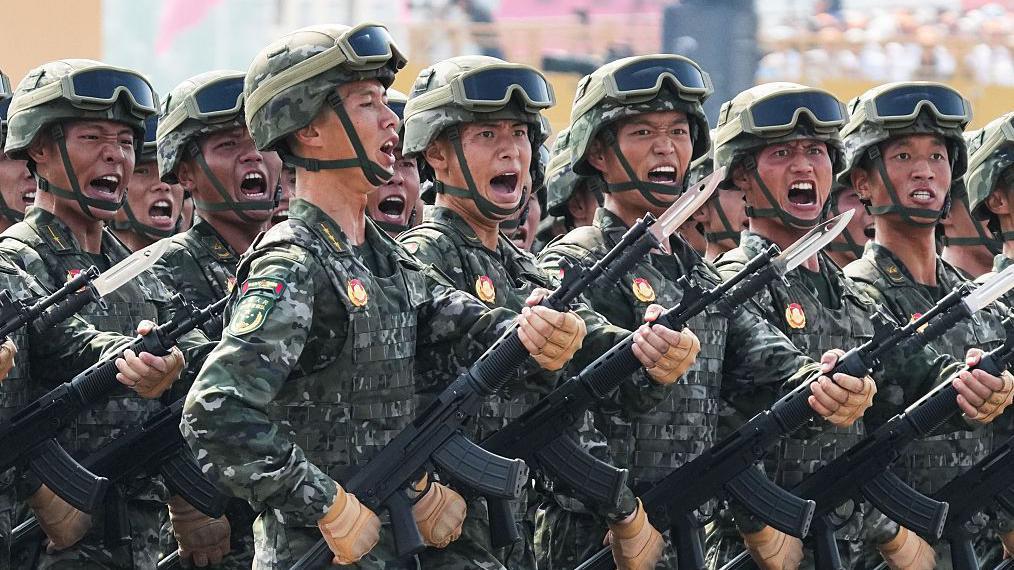一群男子身穿作戰迷彩服，近距離畫面中手持武器一同行進。許多人看起來像是在吶喊。