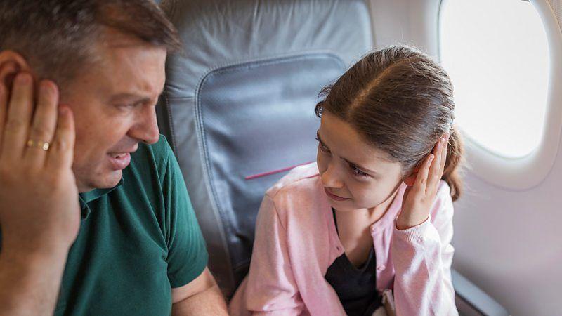 Duas pessoas em um avião, colocando as mãos nos ouvidos