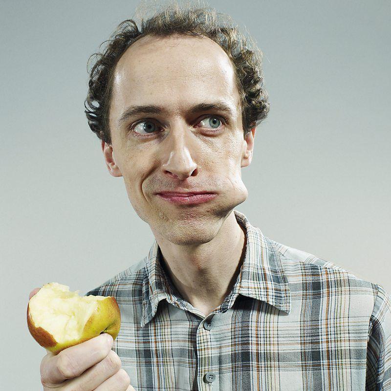 Homem comendo ma&ccedil;&atilde; e olhando para o lado, com um peda&ccedil;o da fruta na boca