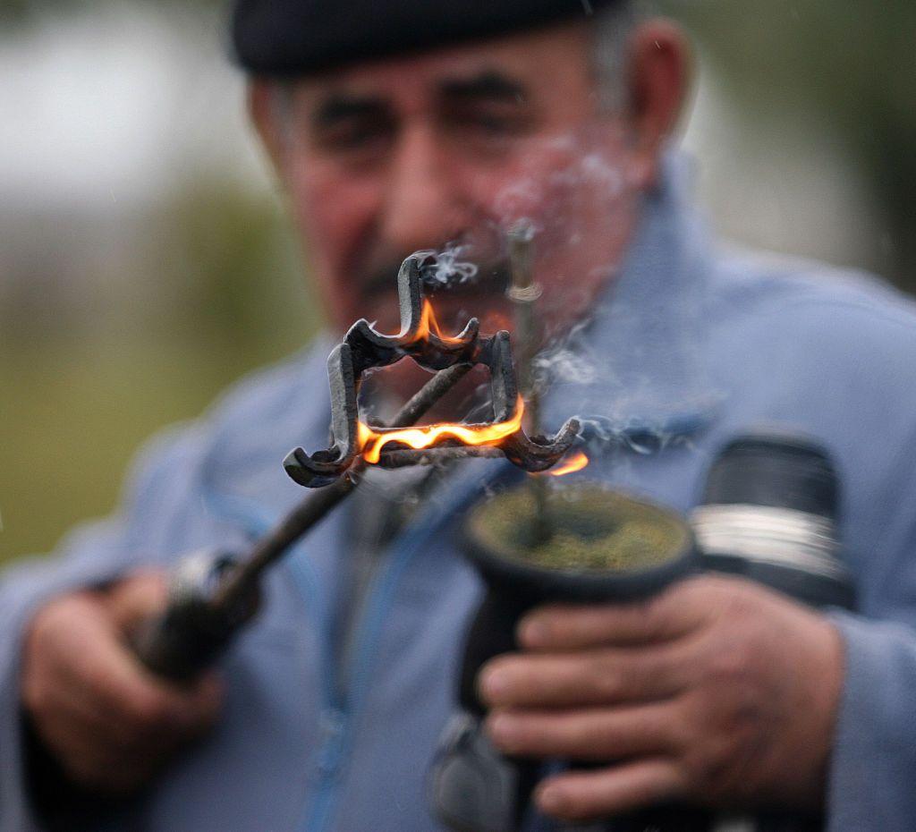 Un hombre con una marca de hierro encendida fuego en una mano y un mate en la otra, con un termo bajo el brazo.