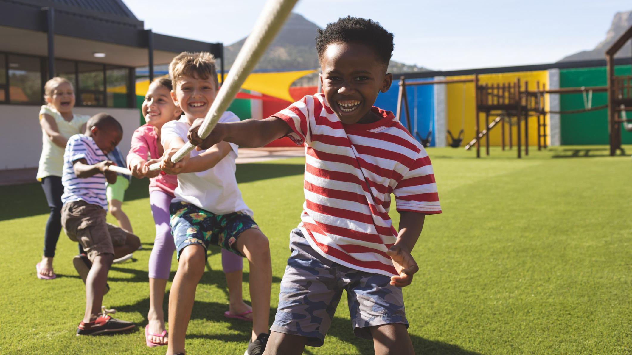Um grupo multi&eacute;tnico de crian&ccedil;as em idade escolar brinca de cabo de guerra em um parquinho