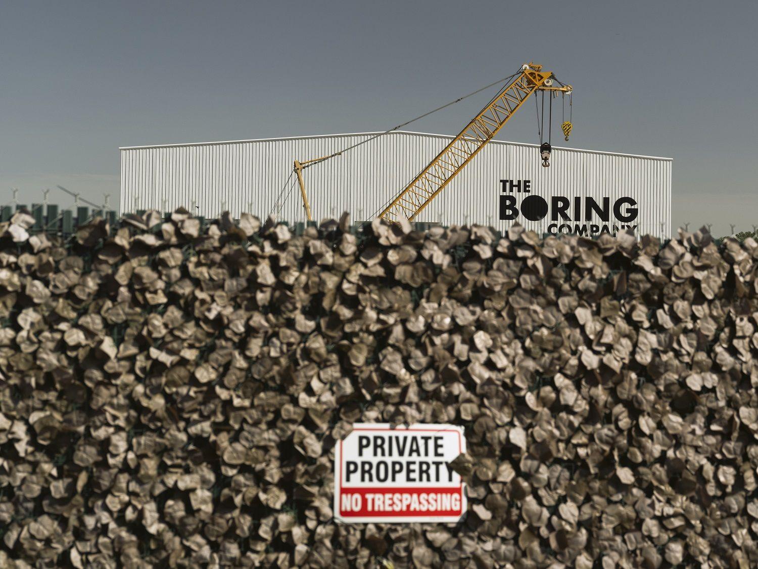Uma vista do prédio da Boring Company com uma parede em primeiro plano, incluindo uma placa que diz