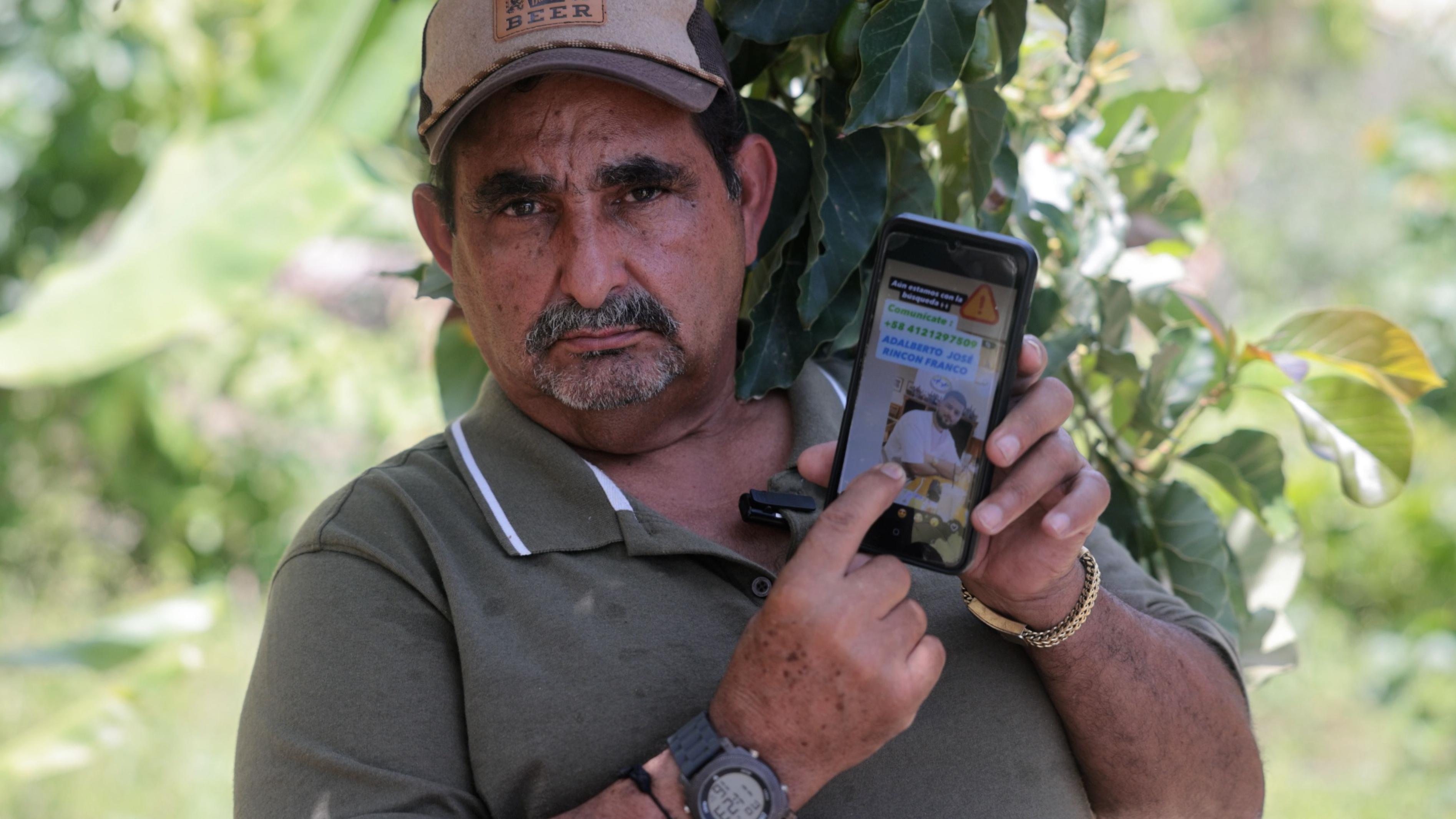 José Rincón mira a cámara y muestra en la pantalla del celular la foto de su nieto Abelardo Rincón, quien regresaba deportado de Estados Unidos a Venezuela en el vuelo 164, en La Guaira, Venezuela, julio de 2026.