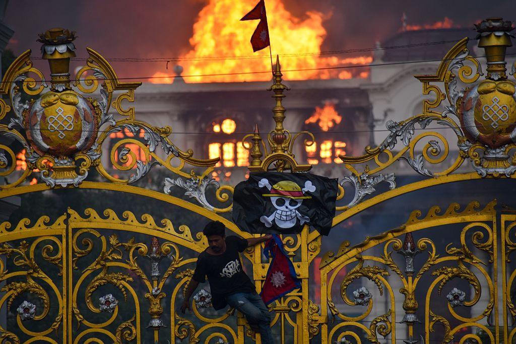 Seorang demonstran memanjat gerbang pintu DPR di Nepal sembari memasang bendera Nepal dan bendera anime One PIece, pada Selasa (09/09).