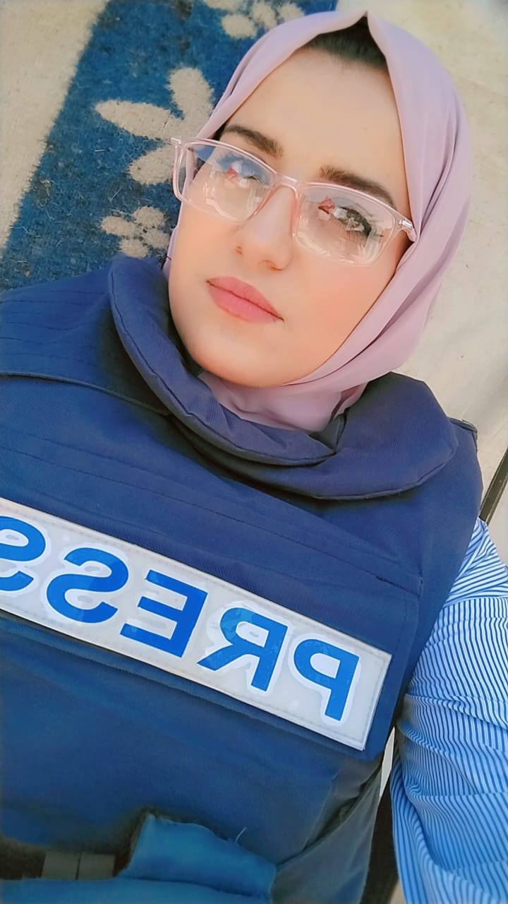 صورة الصحفية حنين حمدونة أمام خيمة ترتدي سترتها الواقية.