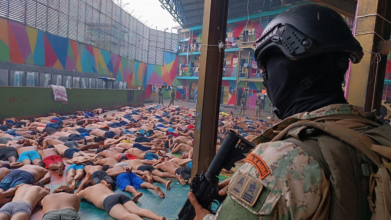 Un militar encapuchado ecuatoriano vigila a un montón de presos acostados boca abajo con el torso desnudo en la Penitenciaría del Litoral, en Guayaquil.