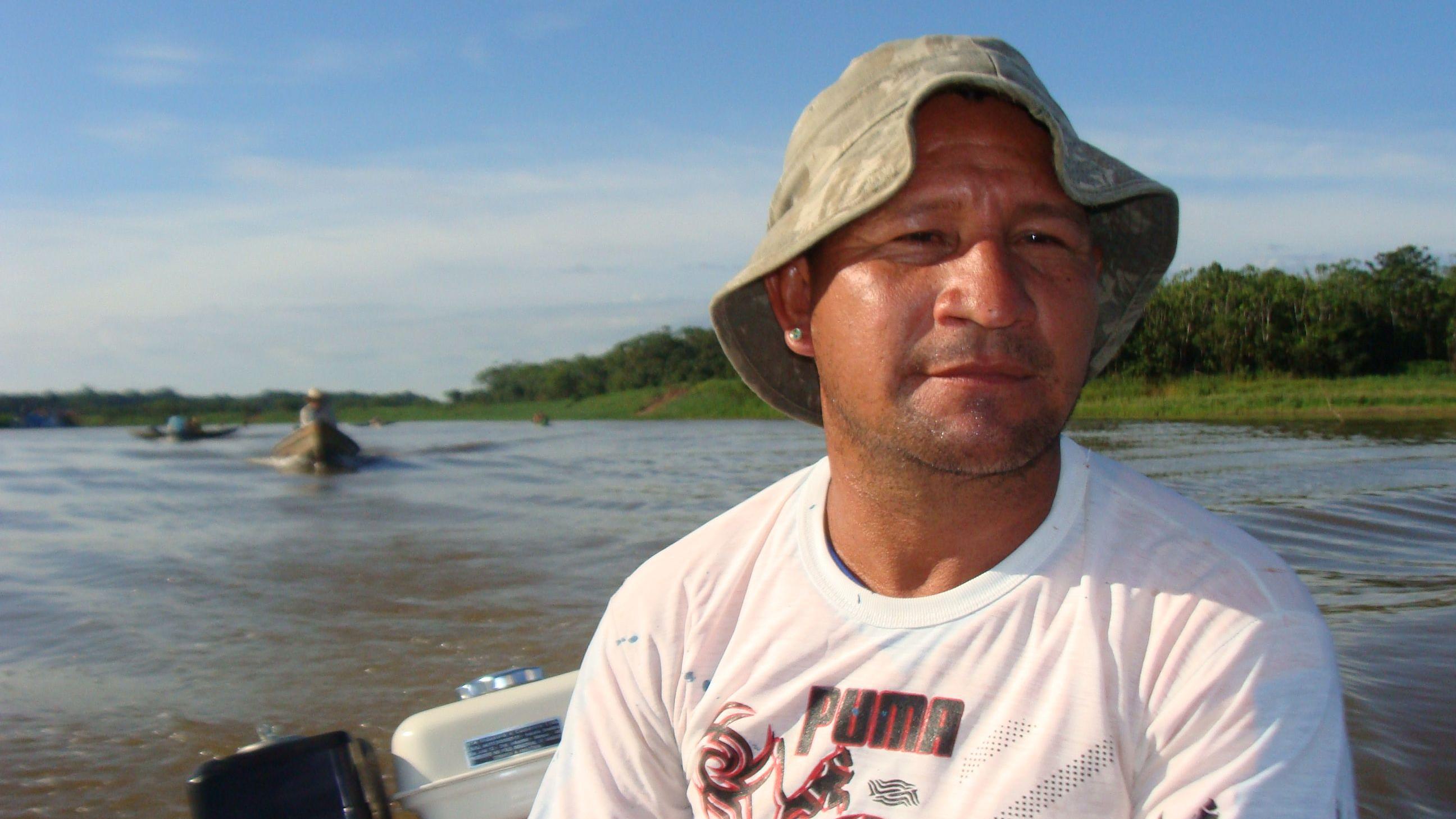 O manejador Pedro Canízio em um barco, com camiseta da maca Puma e um chapéu de pescador