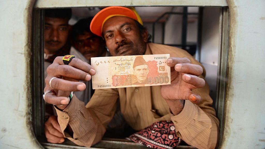 ایک شخص پانچ ہزار روپے کا نوٹ دکھا رہا ہے