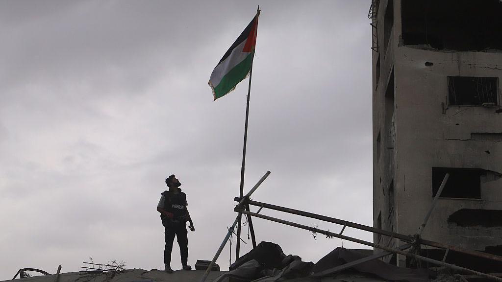 Homem com jaleco olha para um edif&iacute;cio destru&iacute;do na Faixa de Gaza