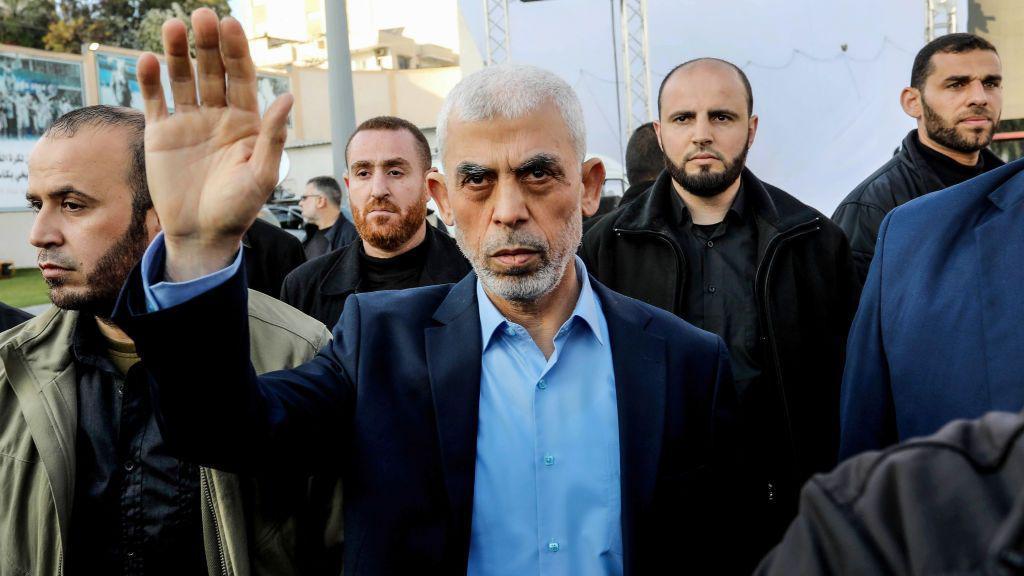 Yahya Sinwar, com um dos bra&ccedil;os para o alto, rodeado de integrantes do Hamas. Ele veste uma camisa azul clara e um terno azul. Todos os homens vestem roupas civis.