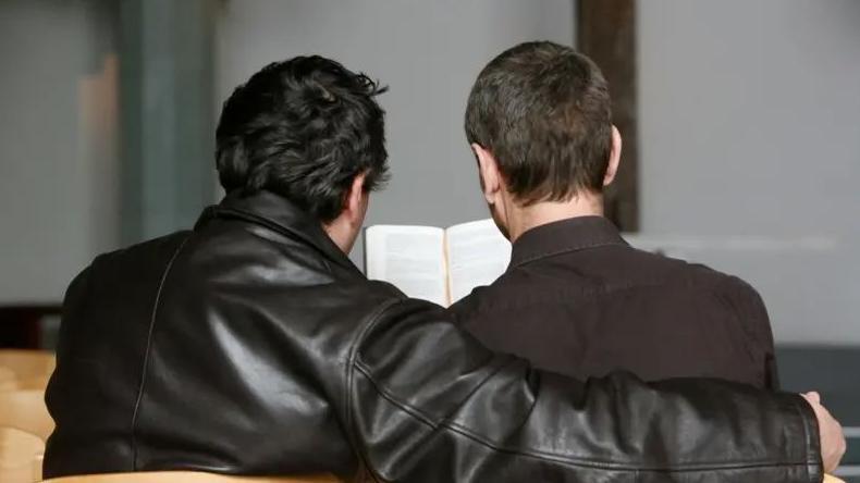 Una pareja de hombres abrazados leyendo la biblia