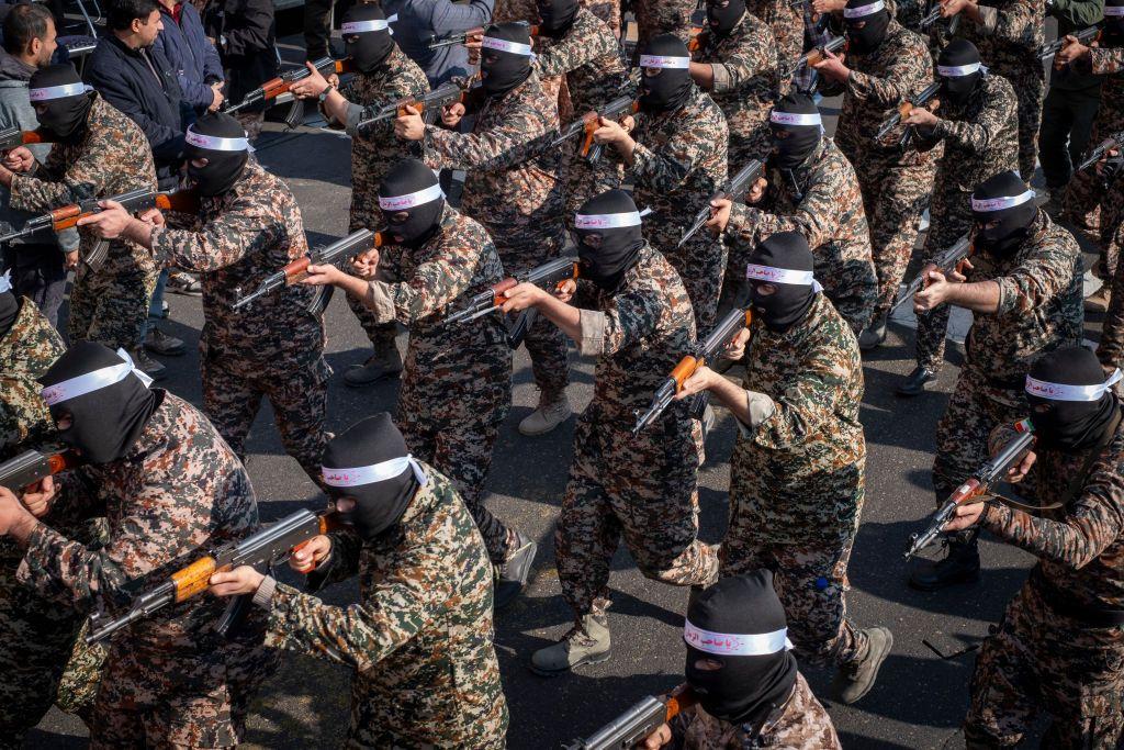 V&aacute;rios membros do IRGC em roupas militares e balaclavas pretas apontam suas armas durante um exerc&iacute;cio.