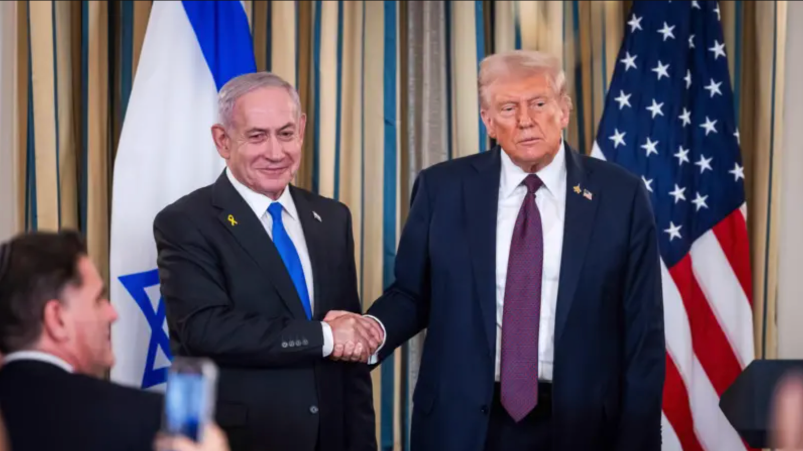 O presidente dos EUA, Donald Trump (direita), cumprimenta o primeiro-ministro israelense Benjamin Netanyahu (esquerda) diante de suas respectivas bandeiras nacionais na Casa Branca em 29 de setembro de 2025.