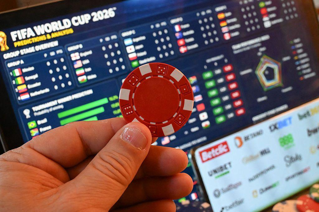 Ilustración de una ficha de casino delante de una pantalla con datos sobre apuestas deportivas relacionados con el Mundial de la FIFA 2026