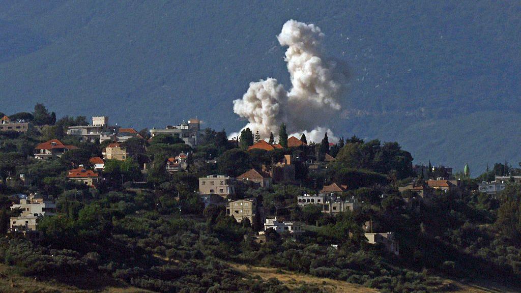 Fuma&ccedil;&atilde; por tr&aacute;s de casas e pr&eacute;dios em montanha arborizada no L&iacute;bano