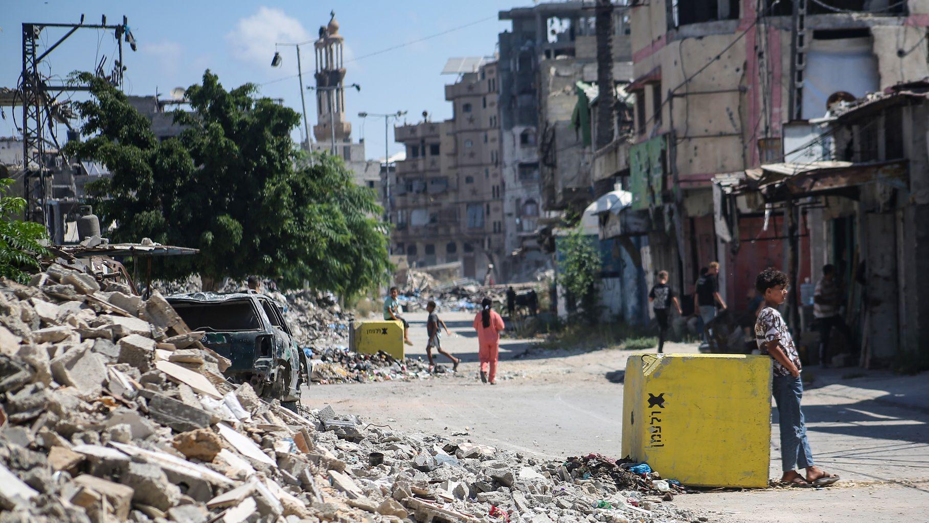 فلسطينيون يسيرون في شارع مليء بالأنقاض بجوار كتلة خرسانية صفراء تُشير إلى "الخط الأصفر" في 27 يوليو/تموز 2026 في حي التفاح بمدينة غزة. 