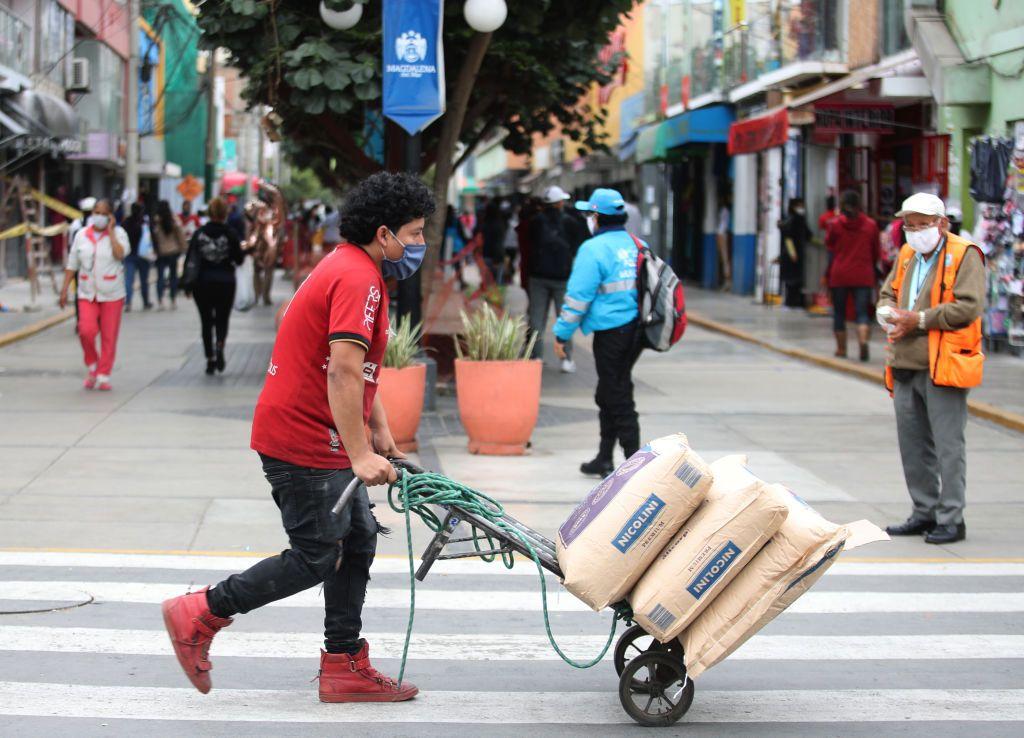 Un hombre empuja un carro cargado con sacos en una concurrida calle de Lima. 