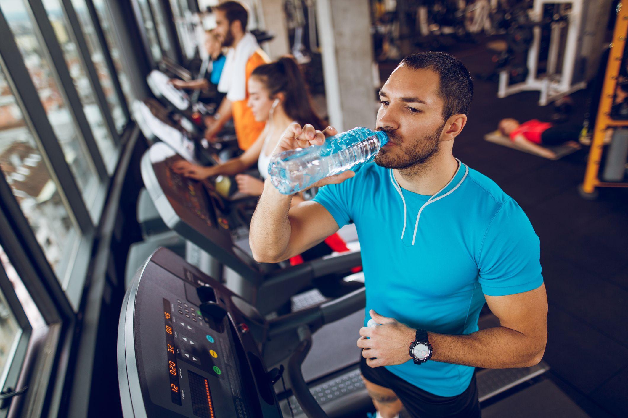 Varias personas haciendo ejercicio en un gimnasio donde un hombre bebe agua.