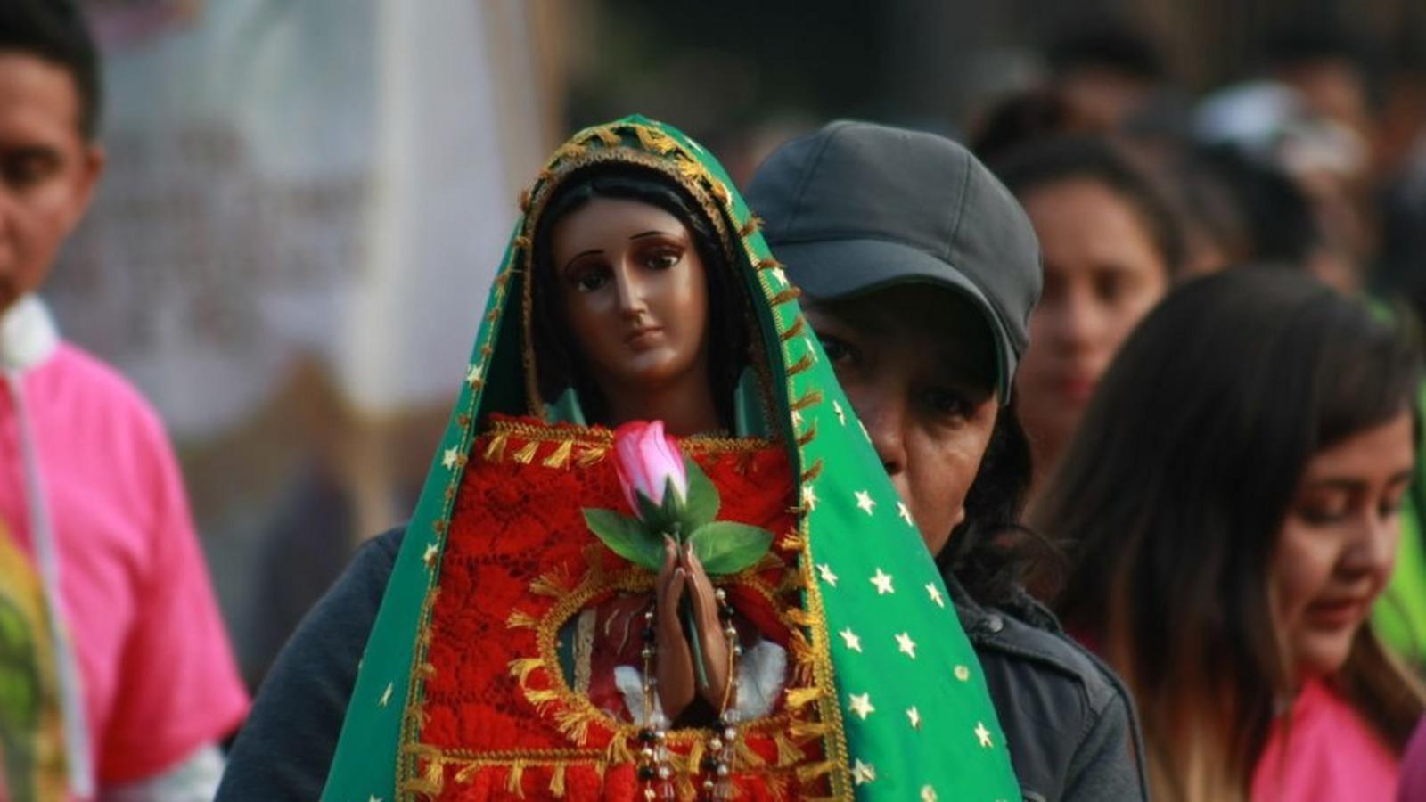 Una mujer con un gorro negro sostiene una efigie de la Virgen de Guadalupe