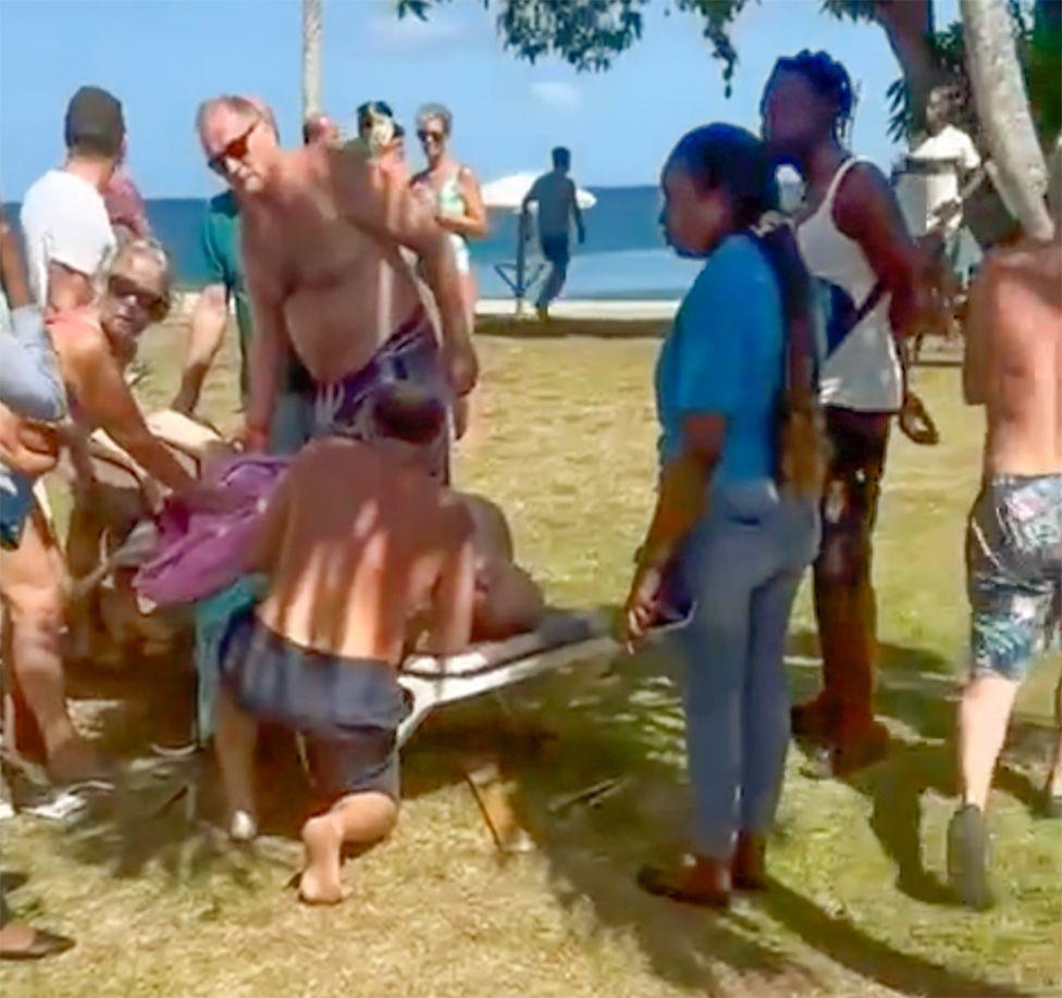 Peter Smith deitado na praia ap&oacute;s o ataque, cercado por pessoas