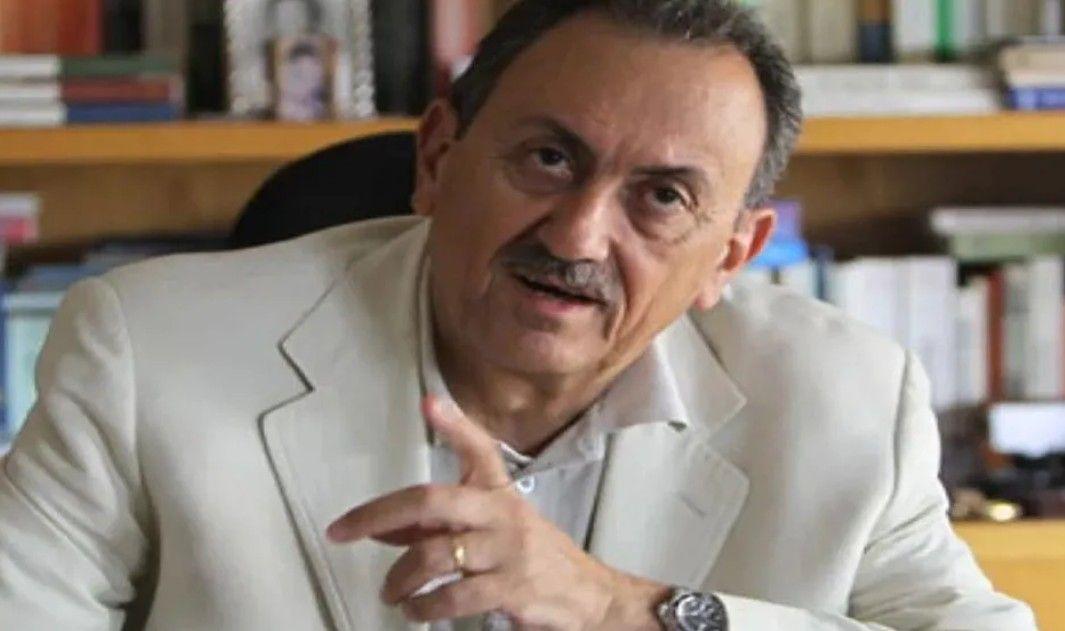 سيمون كرم يرتدي بدلة رسمية بيضاء اللون وخلفه مكتبة صغيرة