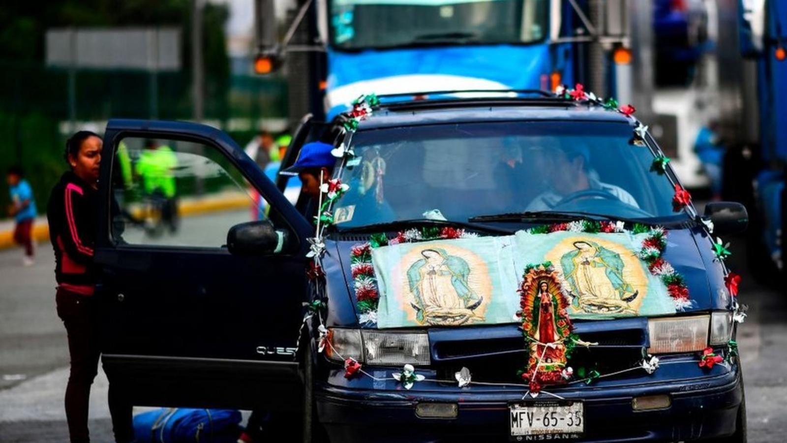 Un automóvil azul, decorado con luces, guirnaldas y varias imágenes de la Virgen de Guadalupe