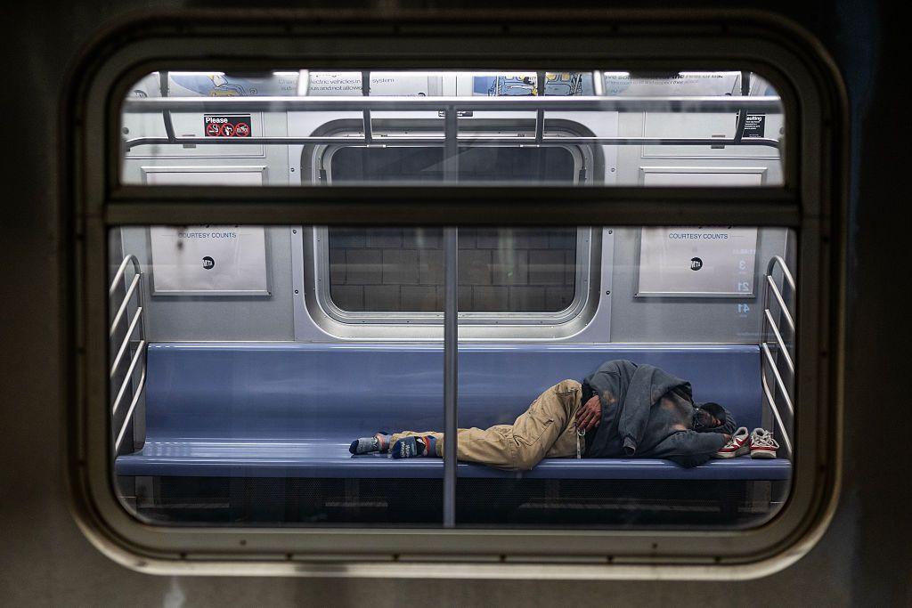 Un hombre sin hogar dormido en un vagón tumbado y dormido en el asiento de un vagón de metro parado en la estación Jamaica Center del metro de Nueva York, una de las líneas de metro más utilizadas por los neoyorquinos sin hogar para refugio, en Queens, Nueva York, el lunes 7 de abril de 2025. (Fotógrafo: Victor J. Blue para The Washington Post a través de Getty Images)