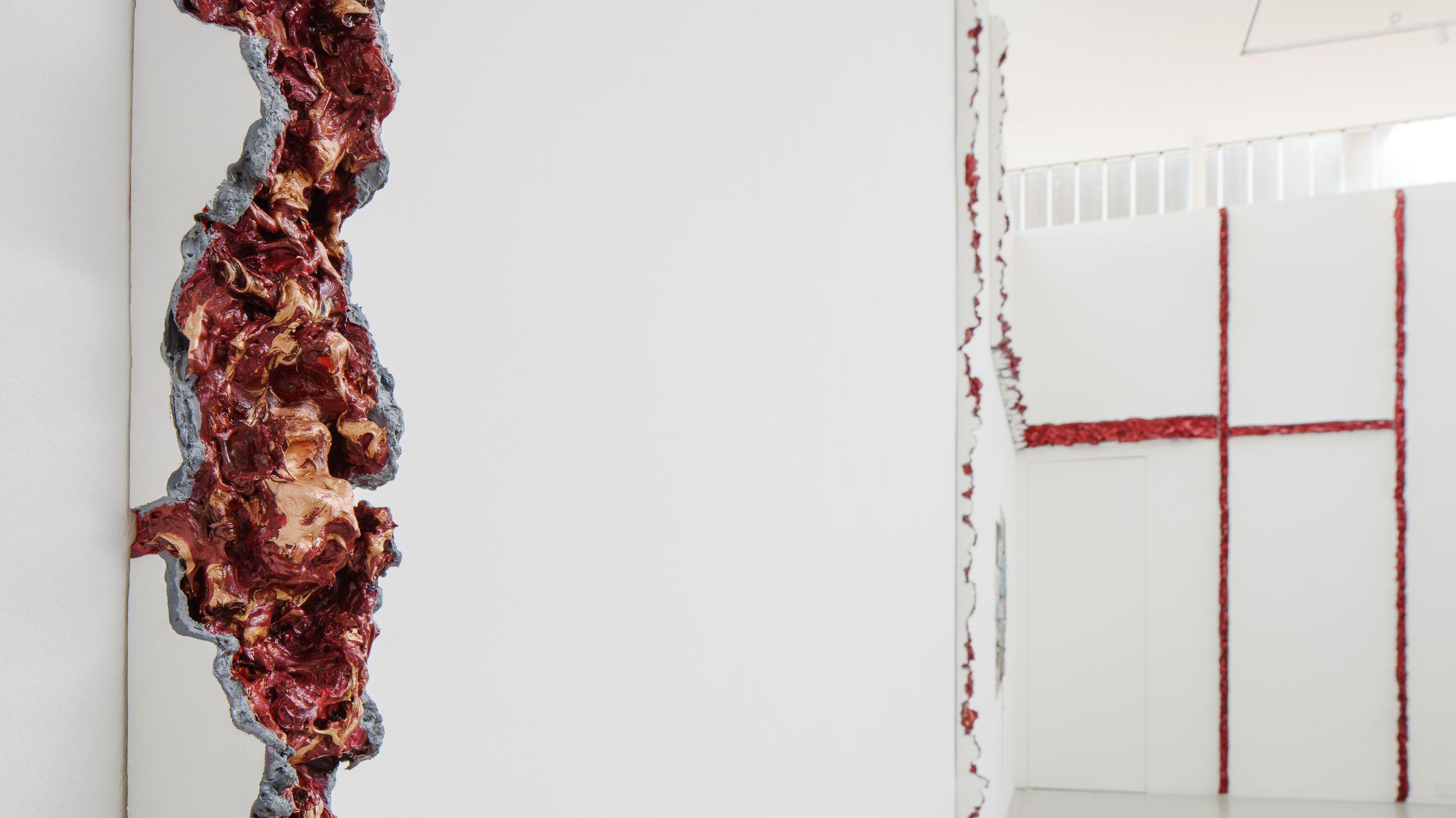 Uma instala&ccedil;&atilde;o art&iacute;stica ocupa paredes brancas com rasgos verticais preenchidos por formas avermelhadas e org&acirc;nicas que lembram carne exposta.