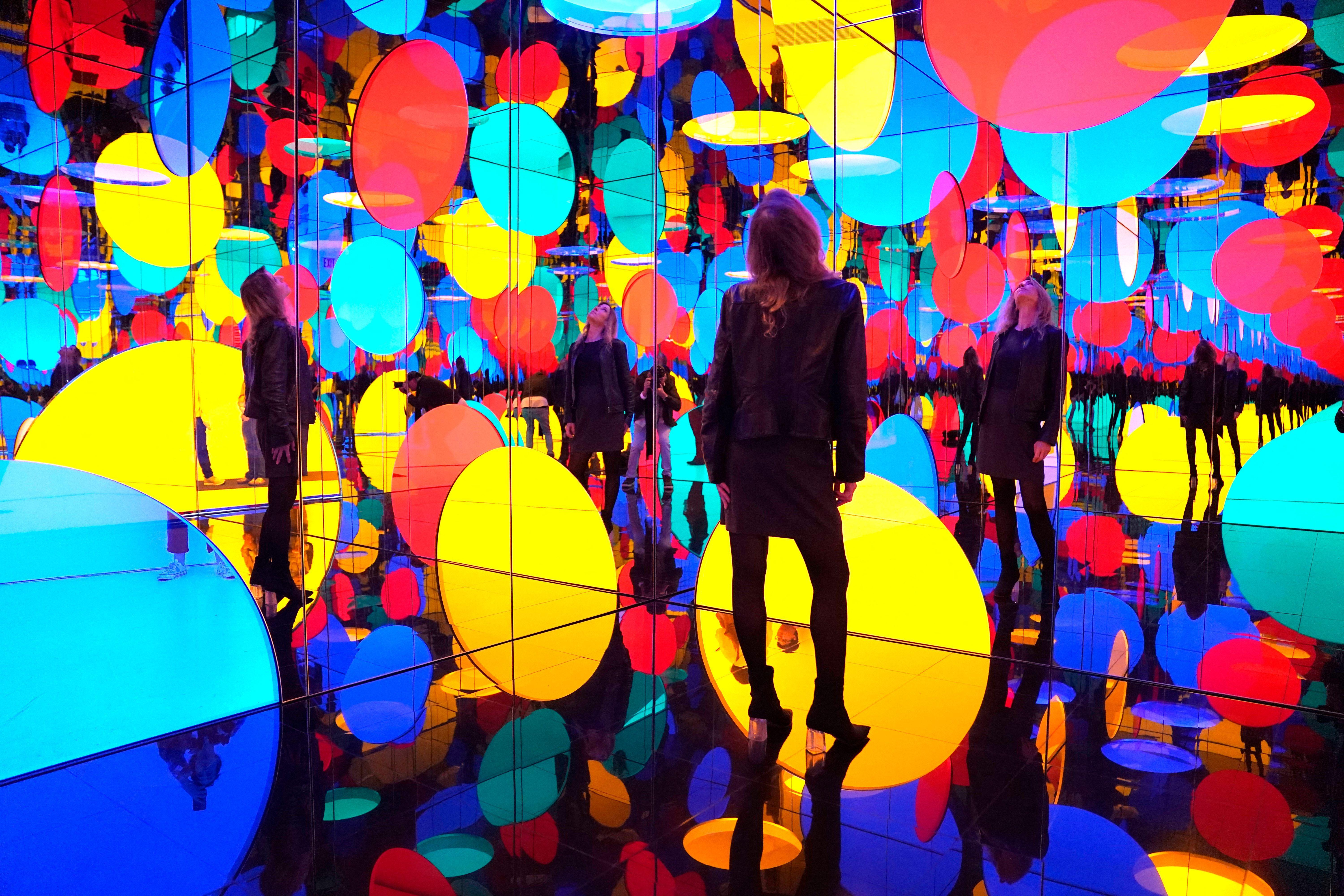 Un visitante de la galería se encuentra en una sala con espejos que contiene muchos círculos de colores brillantes y sus reflejos.