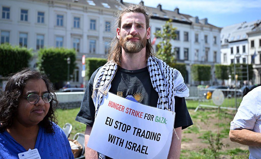 متظاهر أوروبي يحمل لافتة كتب عليها "المجاعة تضرب غزة. أيها الاتحاد الأوروبي! أوقف التجارة مع إسرائيل"، وذلك في وقفة احتجاجية في أمام البرلمان الأوروبي في يونيو/حزيران ٢٠٢٥ في بروكسل، بلجيكا.