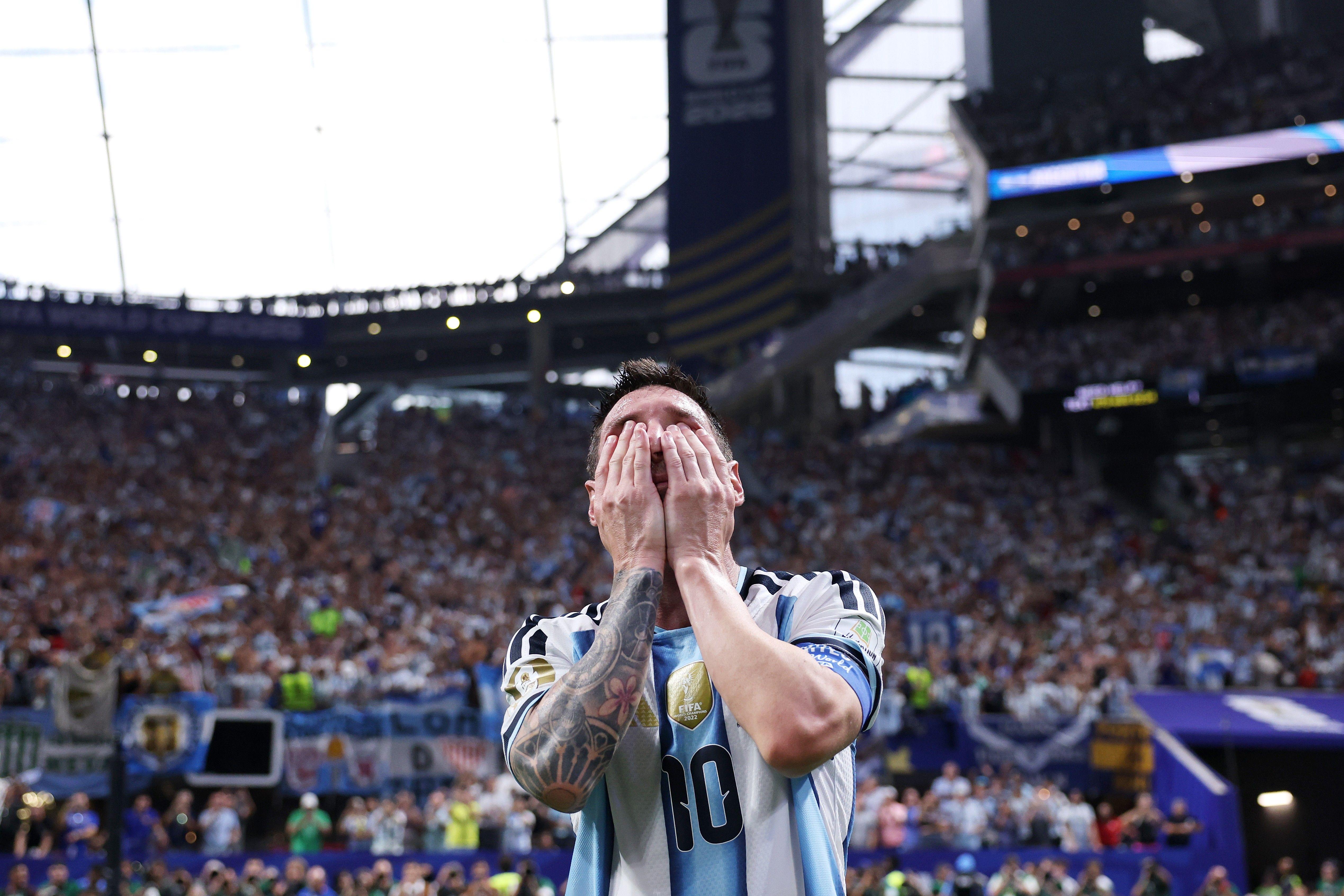 Messi con las manos sobre su rostro, y una tribuna del estadio repleta de aficionados detrás.