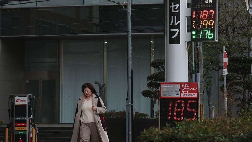 3 月 13 日，在日本神戶，一名女子走過加油站外顯示汽油價格的招牌。