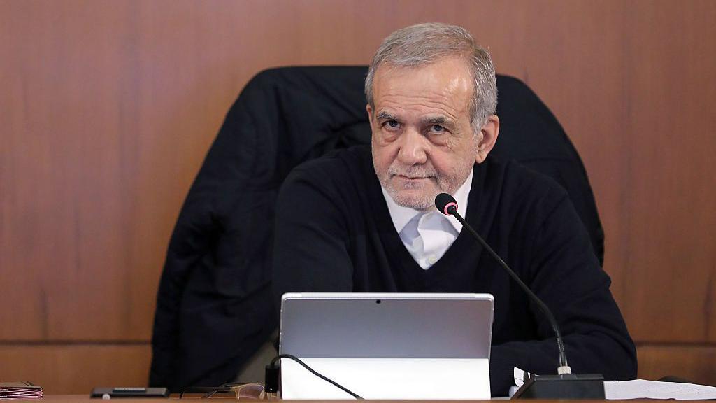 El presidente de Irán, Masoud Pezeshkian, con gesto serio, ante un micrófono en una mesa