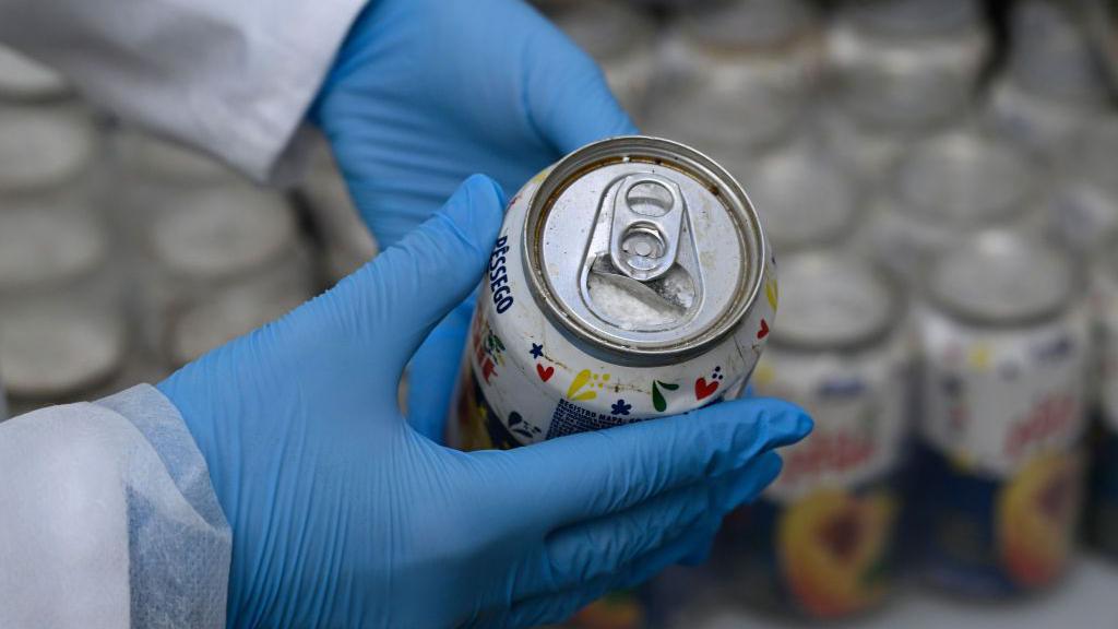 Membro da Pol&iacute;cia Judici&aacute;ria portuguesa mostra uma lata aberta de suco de p&ecirc;ssego confiscada que cont&eacute;m coca&iacute;na, no dia 20 de maio de 2024, em Lisboa, Portugal