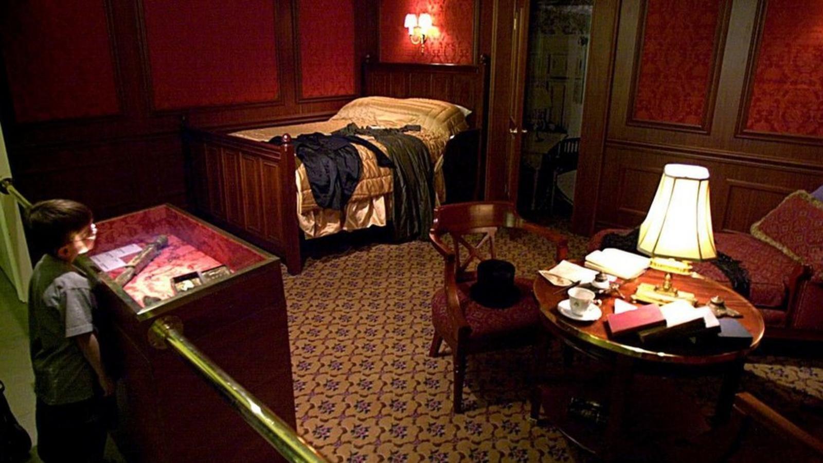 Un niño observa destrás de una barrera una exposición en un museo de un camarote de barco antiguo, enchapado en madera, con una cama, una mesa redonda con una lámpara, libros y una taza de té y dos asientos a su alrededor