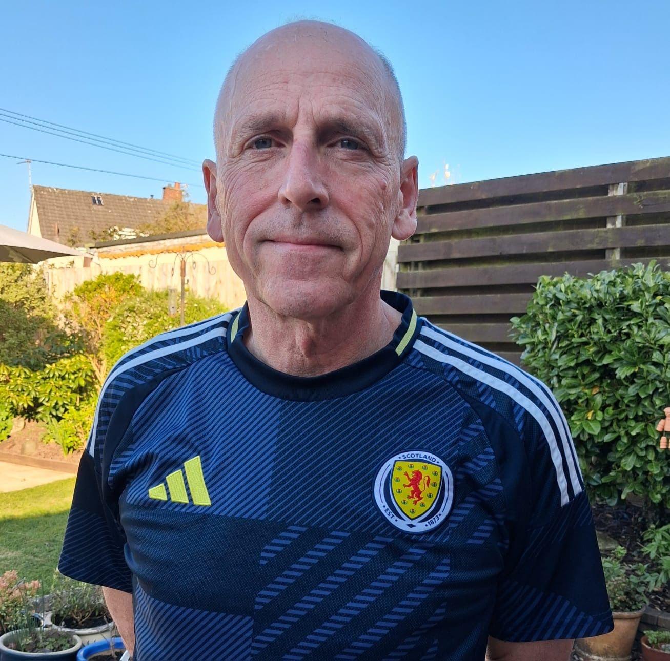 Hamish Husband, vistiendo una camiseta de fútbol escocesa y de pie en su jardín.