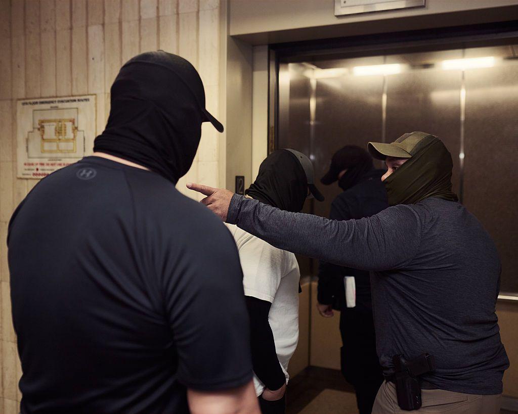 Cuatro agentes migratorios con las caras tapadas entran en un ascensor. 