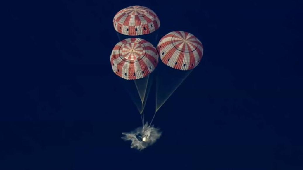 La cápsula Orión ameriza asistida por tres paracaídas de colores rojo y blanco.