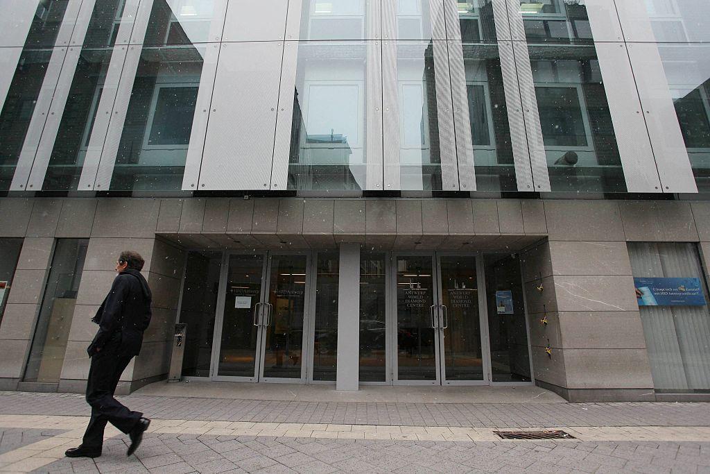 Fachada moderna de vidrio y concreto con varias puertas de entrada y una persona caminando por la acera