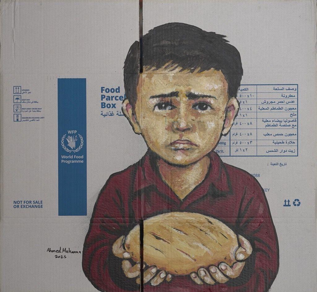رسم لطفل يرتدي قميصاً خمري اللون وجهه عابس ويحمل بكلتا يديه كسرة خبز على لوحة رسمت من كرتونة مساعدات يظهر عليها شعار برنامج الأغذية العالمي. وباللغة الإنجليزية كتب على كرتونة المساعدات باللون الأزرق وباللغة الإنجليزية "ليس للبيع أو للبدل".