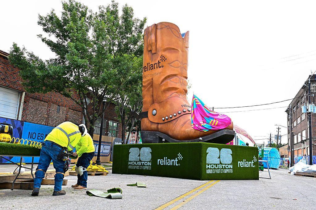 Una calle en Houston, Texas en la que se está instalando una zona para que fanáticos del fútbol puedan disfrutar los partidos. Hay ds trabajadores instalando unas mesas y detrás de ellos se ve una inmensa bota texana de adorno que está instalada en la mitad de la calle