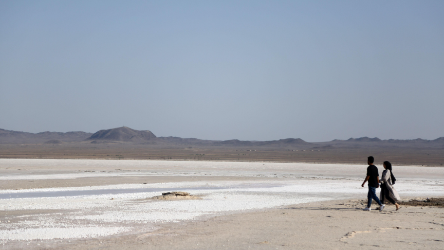 رجل وامرأة يمشيان على قاع بحيرة حوض سلطان في منطقة قُم – ويمكن رؤية الملح على سطح القاع"