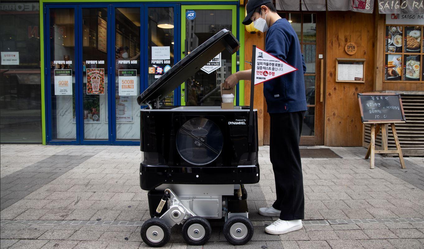 Un empleado de una cafetería coloca tazas de café en un robot de reparto de Robotis Co.