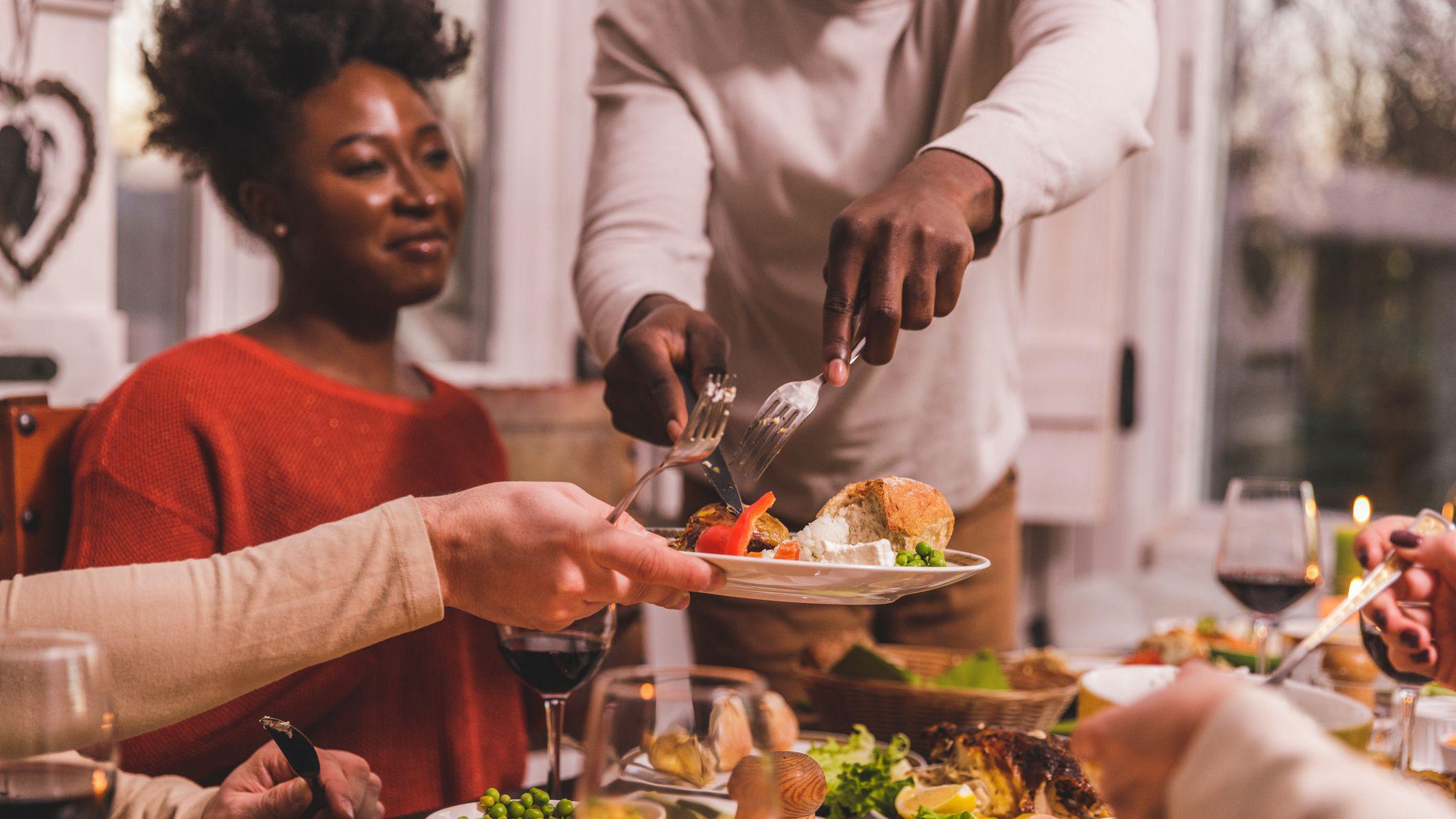 Pessoas à mesa em uma refeição, com um homem servindo um pedaço de ave para outra pessoa